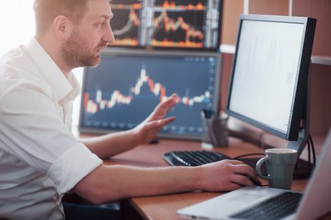 Stockbroker in shirt is working in a monitoring room with display screens. Stock Exchange Trading